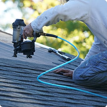 man using a nail gun on a roof.